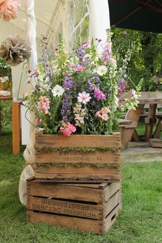 a wooden crate filled with lots of flowers on top of green grass next to a picnic table