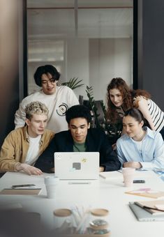 four people sitting around a table looking at a laptop