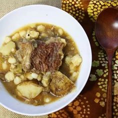 a white bowl filled with stew next to a wooden spoon on top of a table