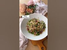 a white bowl filled with food sitting on top of a wooden cutting board next to flowers