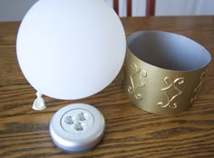 a white light bulb next to a metal container on top of a wooden table with a gold band around it