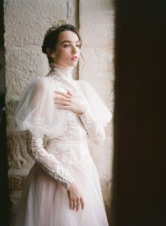 a woman in a white dress standing next to a stone wall wearing a tiara