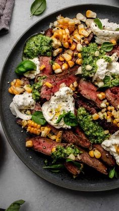 a black plate topped with steak, corn and broccoli on top of a table