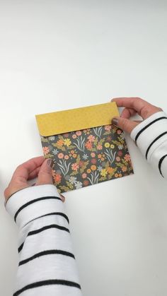 two hands holding an envelope with yellow and black paper on it, while another person holds the envelope