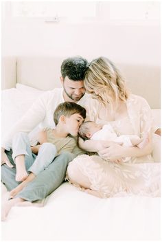 a man, woman and two boys are laying on a bed with their newborn baby