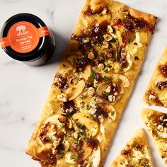 four slices of flat bread with nuts and herbs on them next to a jar of jam