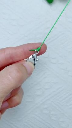 a person is holding a green string with a silver fish charm on it's end