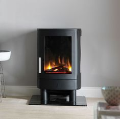 a black stove in a living room next to a chair and table with a vase on it