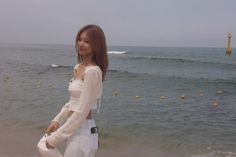 a woman standing on the beach next to the ocean with her hand in her pocket