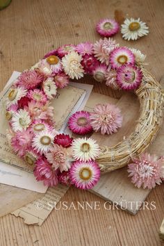 a wreath made out of flowers sitting on top of a wooden table next to an envelope