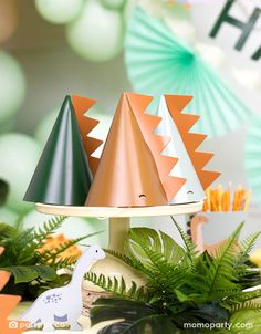 three party hats sitting on top of a table next to green plants and other decorations