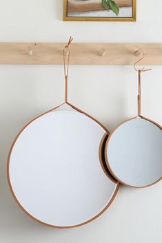 two circular mirrors hanging on a wall near a wooden shelf with a painting above it