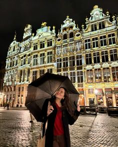 a woman holding an umbrella standing in front of a building with many windows at night