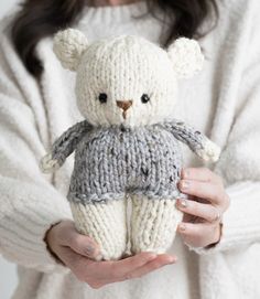 a woman holding a knitted teddy bear in her hands and wearing a white sweater