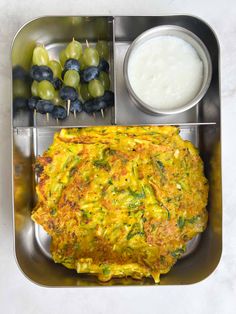 a metal tray filled with food next to a bowl of grapes and yogurt