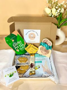 a box filled with various items on top of a white sheet covered table next to a vase