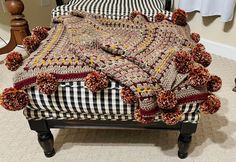 a blanket on top of a footstool with pom poms around it