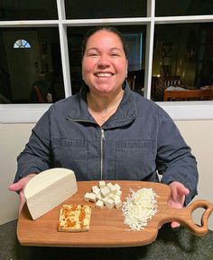 a woman holding a wooden cutting board with cheese on it