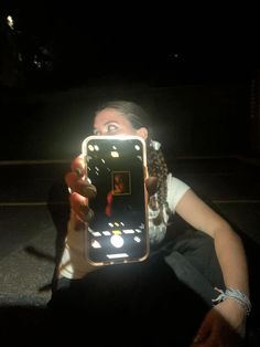 a woman holding up a cell phone with lights on it's screen in the dark