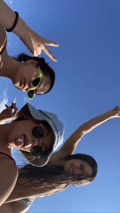 three young women standing next to each other in front of a blue sky with clouds