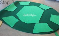 a green turtle made out of felt sitting on the floor next to a pair of scissors