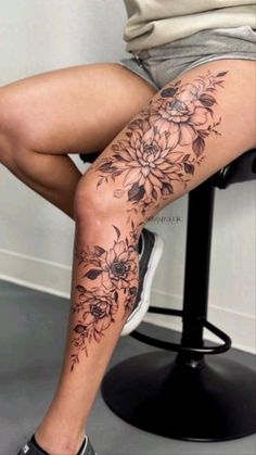 a woman sitting on top of a chair with her legs covered in tattoos and flowers