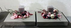 two candles are decorated with christmas ornaments and decorations on concrete block holders, one is pink and the other is grey