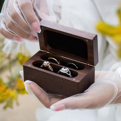 a person holding two rings in a wooden box