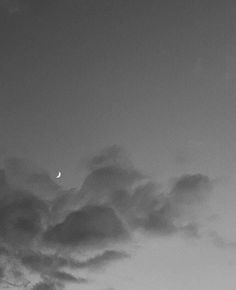 black and white photograph of clouds with the moon in the sky behind them, as seen from an airplane