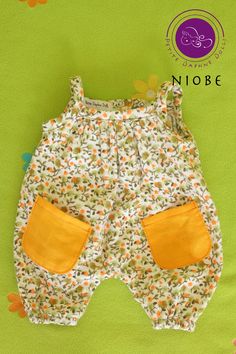 a baby's romper with yellow pockets and flowers on the bottom, sitting on a green surface