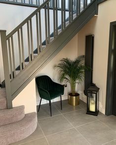 a green chair sitting under a stair case next to a potted plant and lamp