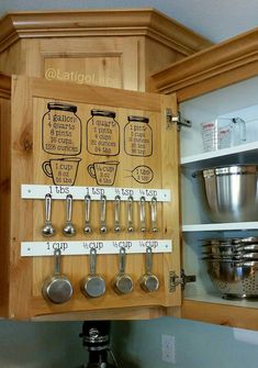 a wooden cabinet with measuring spoons and measuring cups on the bottom, labeled kitchen utensils