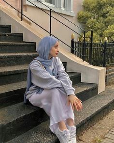 a woman sitting on some steps wearing a hijab and white tennis shoes in front of a building