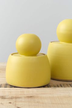 two yellow vases sitting on top of a wooden table next to eachother