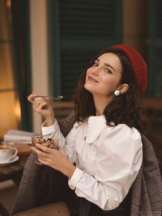 a woman sitting at a table with a bowl of food in her hand and looking up to the sky