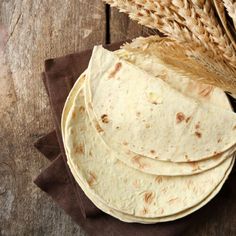 three tortillas on a brown napkin next to some ears of wheat