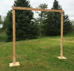 a wooden frame sitting in the middle of a grass covered field with trees behind it