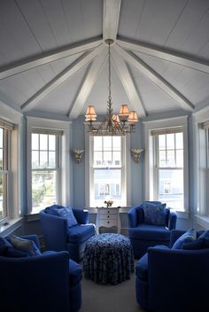 a living room filled with blue furniture and two lamps hanging from the ceiling next to windows