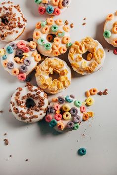 several donuts with cereal and cereal toppings scattered around them on a white surface