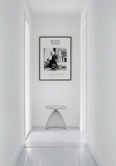 a white hallway with a black and white photo on the wall above a wire table