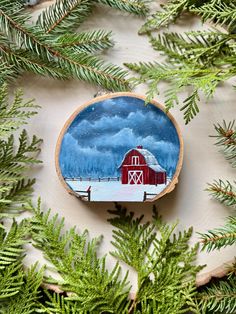 a red barn is painted on a piece of wood surrounded by pine needles and branches