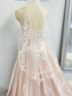 the back of a wedding dress on display in front of a mirror with its veil draped over it