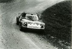 a black and white photo of a race car on a dirt road with trees in the background