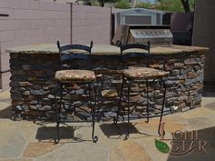 an outdoor bar with four stools and a grill in the back ground, next to a stone wall