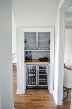 an open refrigerator in the corner of a kitchen with white walls and wood floors, along with a built - in wine cooler