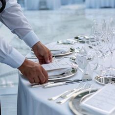 a waiter is setting the table with silverware and place settings for guests to eat