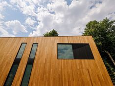 a tall wooden building with three windows on the side and trees in the back ground