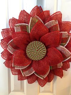 a red wreath with green and white ribbons hanging on the front door, decorated with an ornament