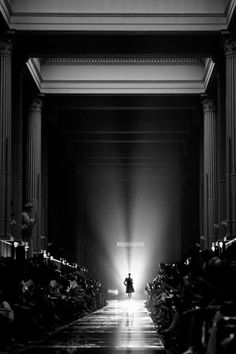 a black and white photo of a person walking down a runway in front of an audience