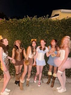 a group of young women standing next to each other on a sidewalk in front of a hedge